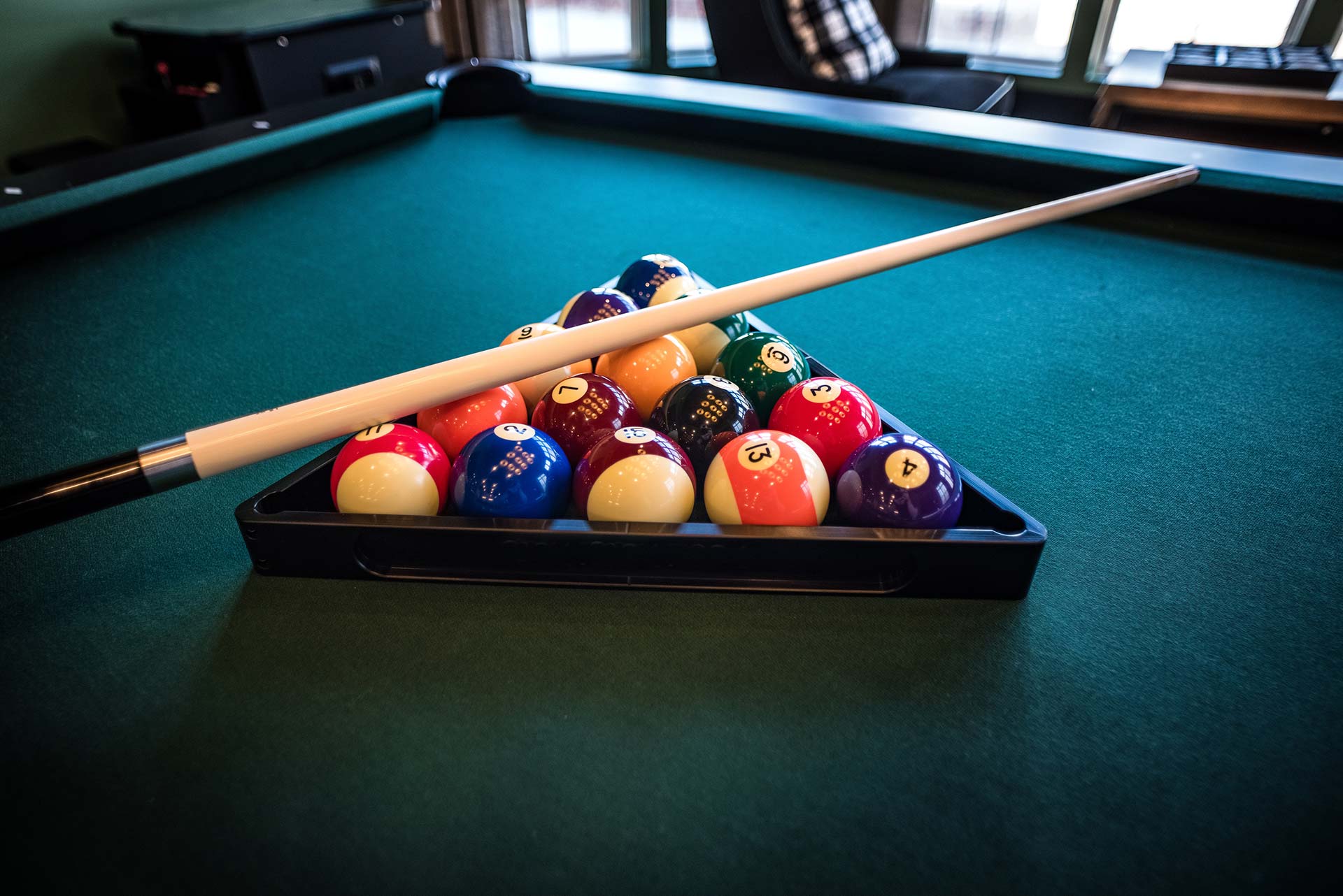 Pool table with balls racked in the triangle and cue resting on top